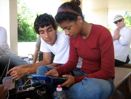 Two high school age students examine an instrument, with an adult in background.