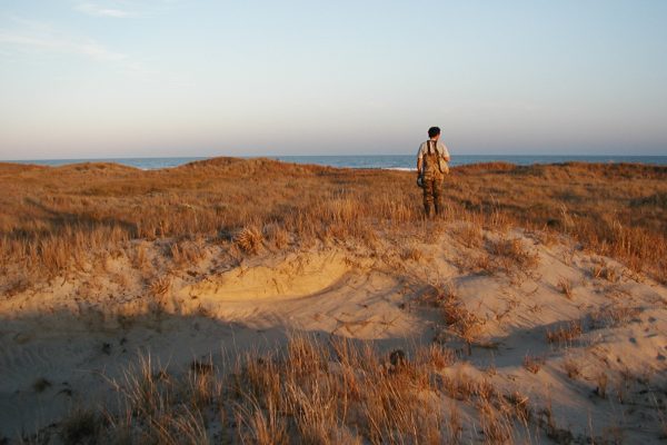 technician standing on dune, facing the ocean