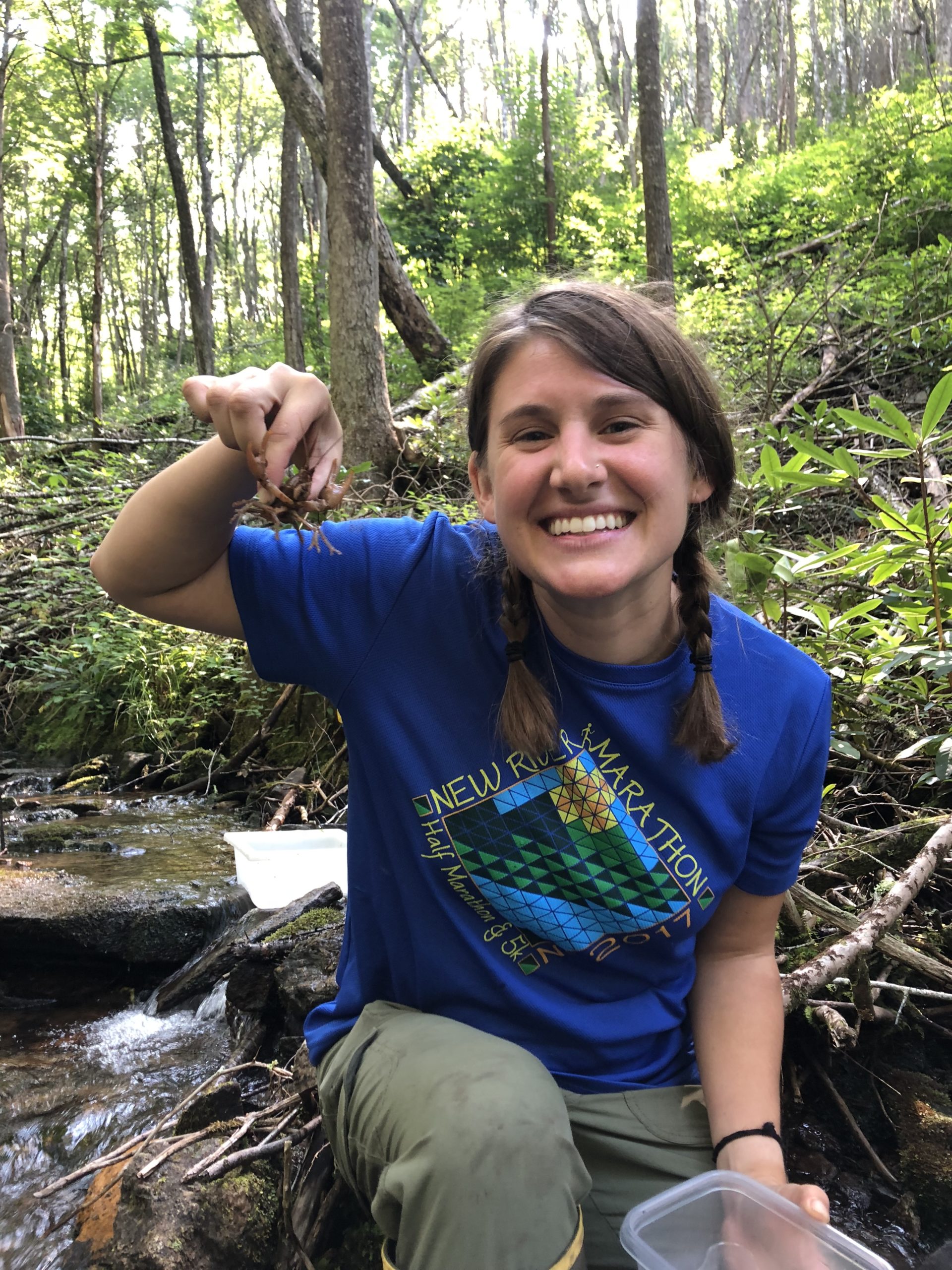 female researcher in creek holding crayfish