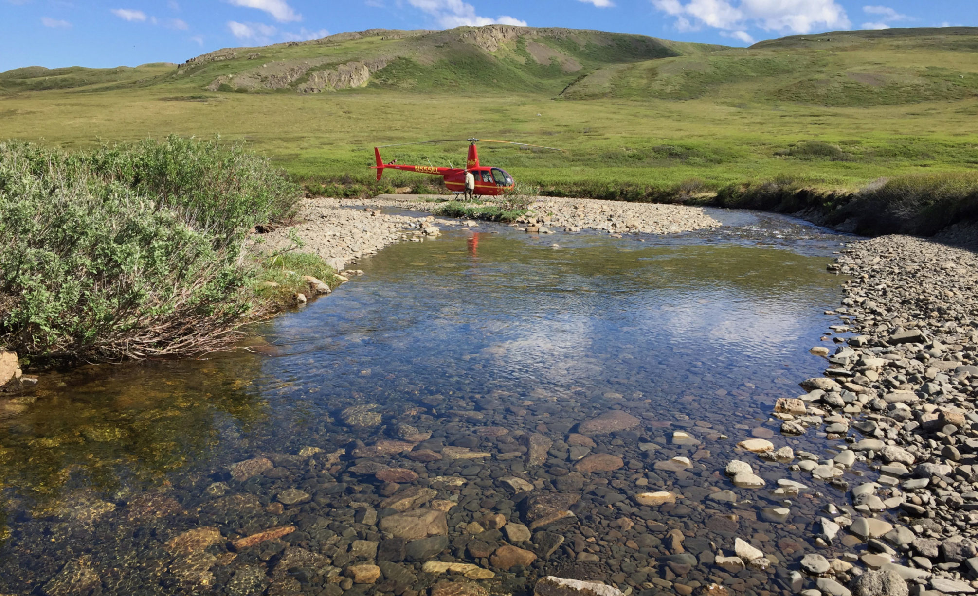 shallow gravelly streambed with helicopter and tussocky hills in the background