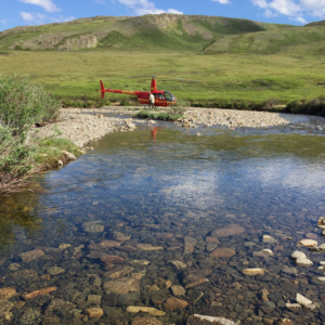 shallow gravelly streambed with helicopter and tussocky hills in the background