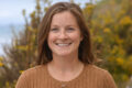 Smiling woman in front of a bluff overlooking the ocean.