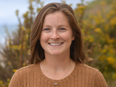 Smiling woman in front of a bluff overlooking the ocean.