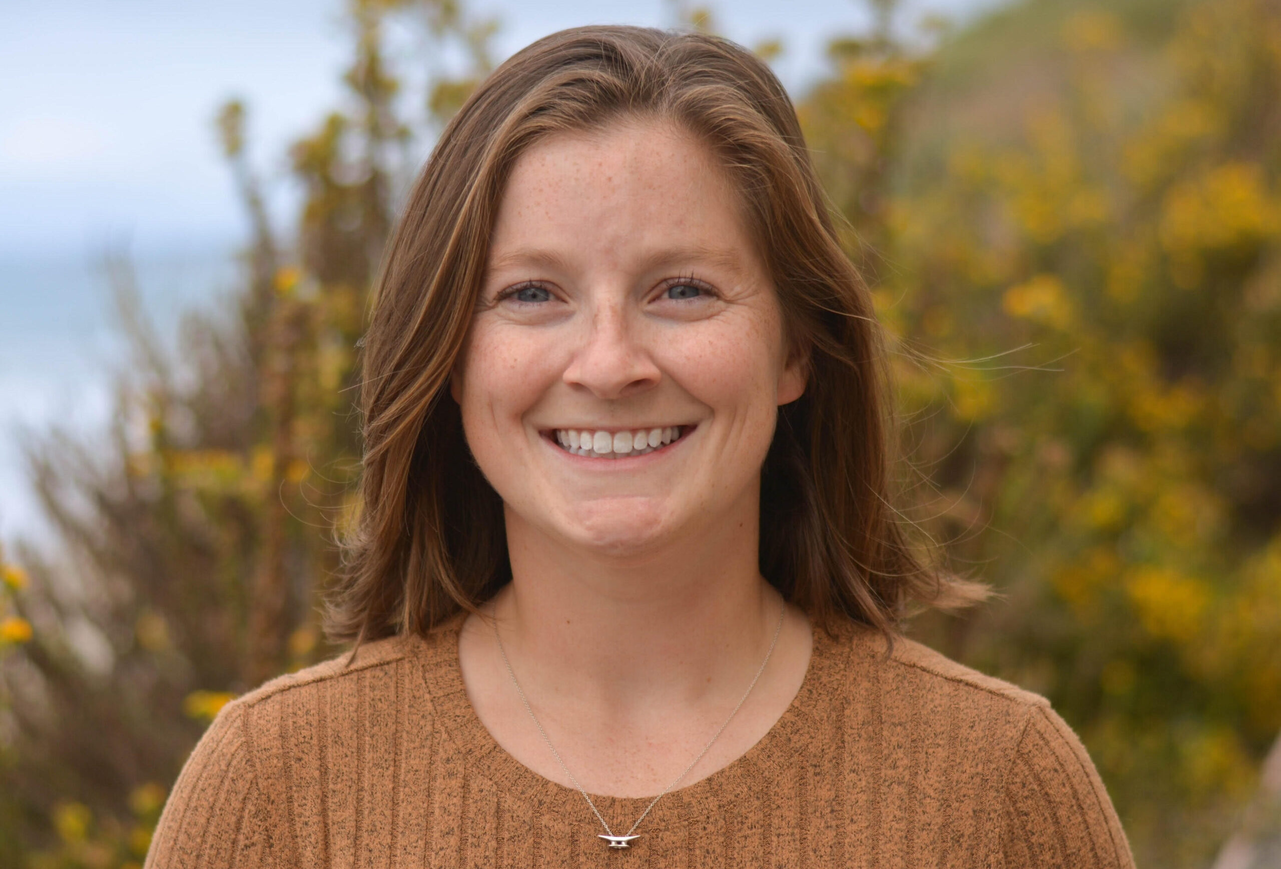 Smiling woman in front of a bluff overlooking the ocean.