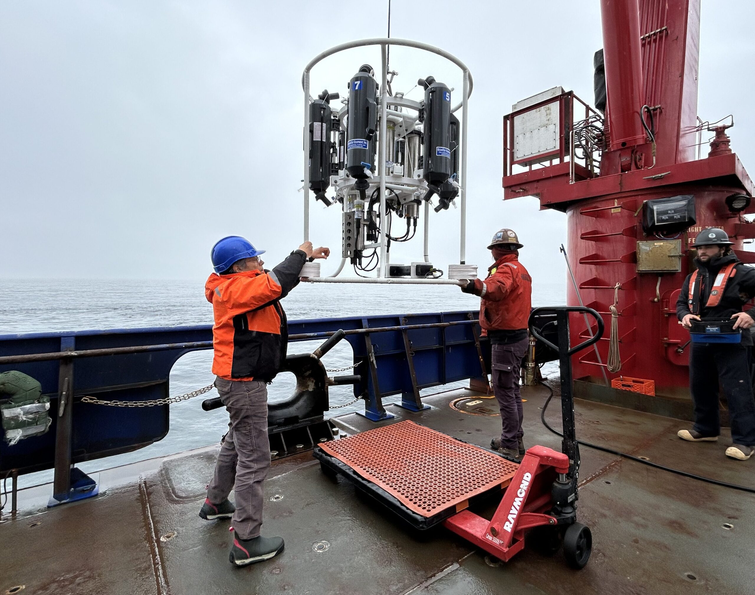 Two oceanographers on the deck of a ship handling a CTD.