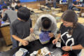 Three students at a lab bench with an urchin in a plastic container and a balance.