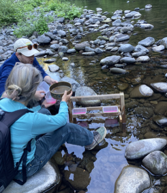 A man and a woman, sieving sediment from a rocky creek bed