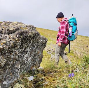 individual with a big pack passing a rocky outcrop in an open landscape