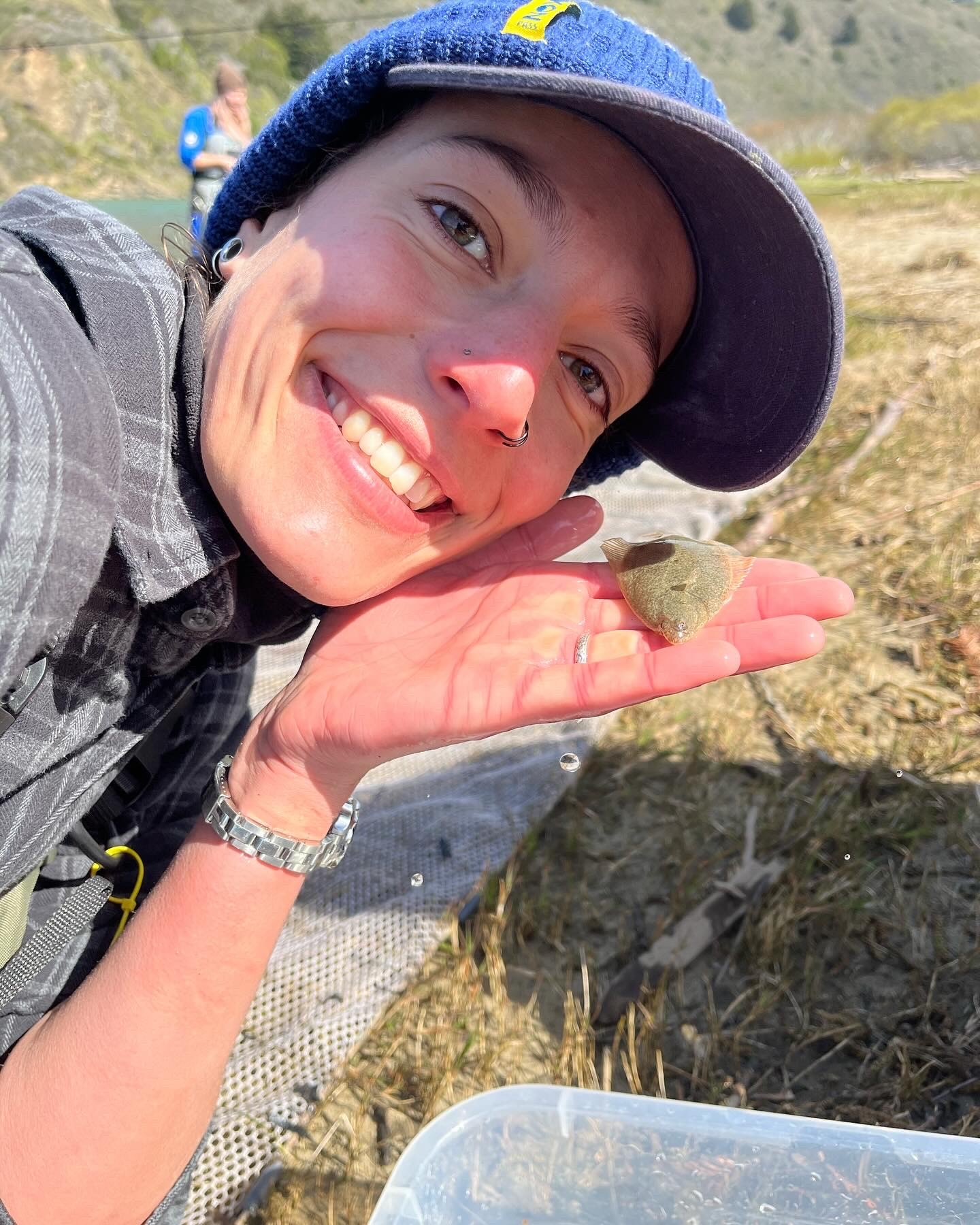 Smiling woman in a marsh with a baseball cap.